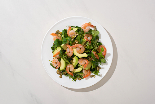 top view of fresh green salad with pumpkin seeds, shrimps and avocado on plate on white background
