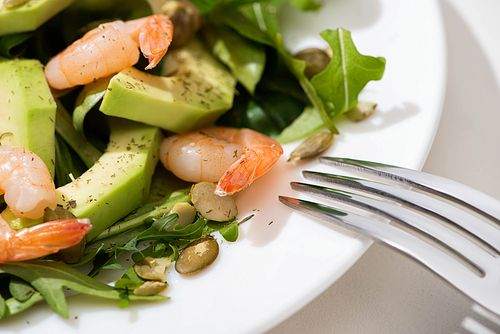 close up view of fresh green salad with pumpkin seeds, shrimps and avocado on plate with fork