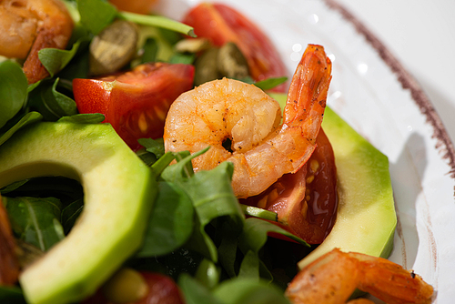 close up view of fresh green salad with pumpkin seeds, cherry tomatoes, shrimps and avocado on plate