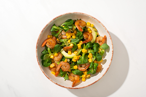 top view of fresh green salad with corn, shrimps and avocado on plate on white background