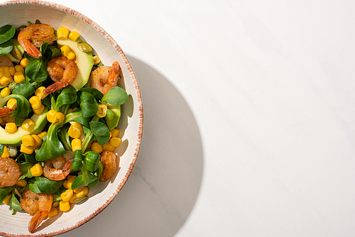 top view of fresh green salad with corn, shrimps and avocado on plate on white background