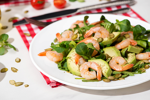 fresh green salad with shrimps and avocado on plate and plaid napkin on white background