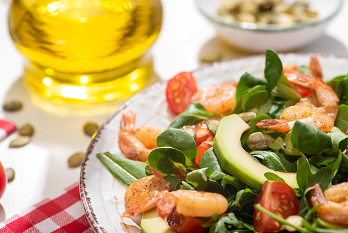 selective focus of fresh green salad with shrimps and avocado on plate and plaid napkin on white background