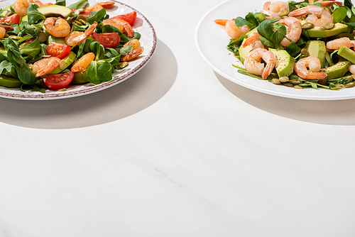fresh green salad with shrimps and avocado on plates  on white background