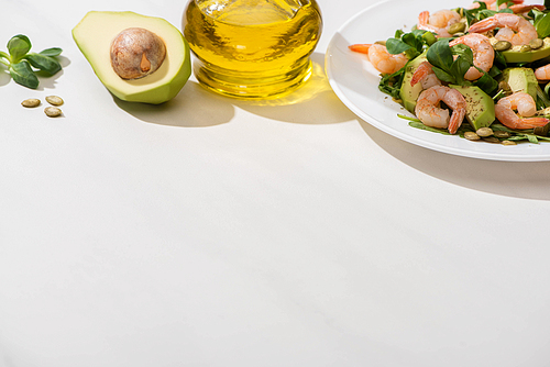 fresh green salad with shrimps and avocado on plate near olive oil on white background