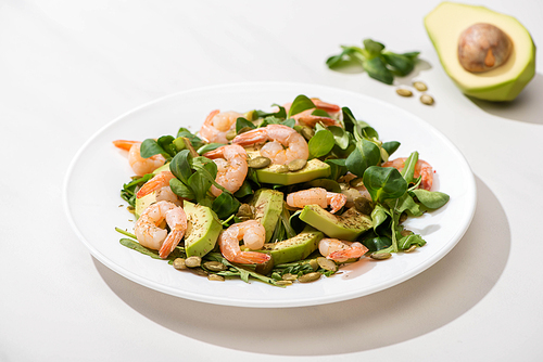 selective focus of fresh green salad with shrimps and avocado on plate on white background