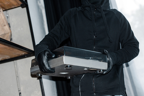 Cropped view of robber in leather gloves holding record player during theft