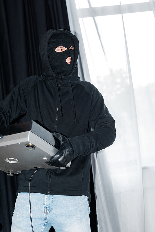 Robber in balaclava and leather glove holding record player during burglary