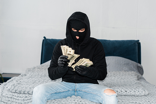 Thief in mask and leather gloves counting dollars on bed