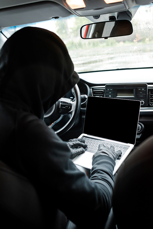 Back view of burglar in leather gloves using laptop with blank screen in auto