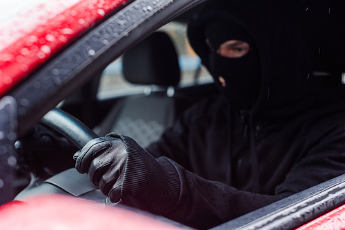 Selective focus of thief in balaclava and leather glove sitting in car