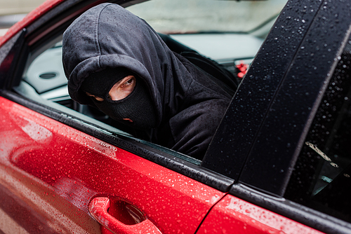 Selective focus of robber in balaclava looking away while sitting in car