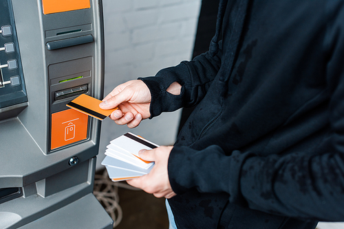 Cropped view of thief holding credit cards near automated teller machine