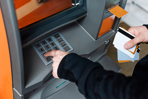 Cropped view of thief using atm while holding credit cards
