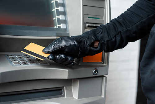 Cropped view of burglar in leather glove holding credit card near atm