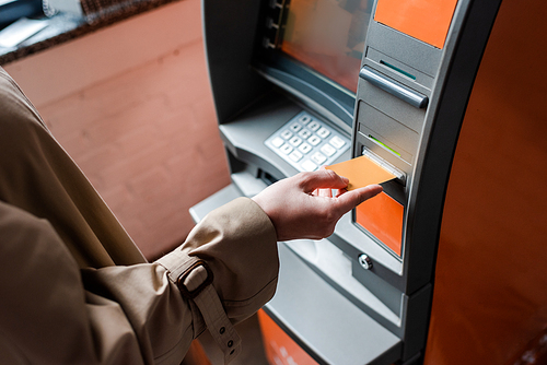 Cropped view of woman holding credit card while using atm