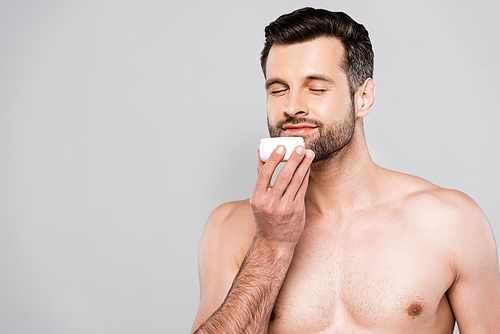 happy bearded man smelling cosmetic cream isolated on grey