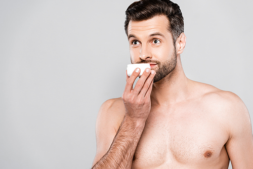 bearded man smelling cosmetic cream isolated on grey