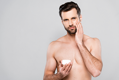 shirtless man holding container while applying cosmetic cream isolated on grey