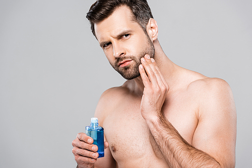 handsome man holding bottle with after shave lotion and touching face isolated on grey