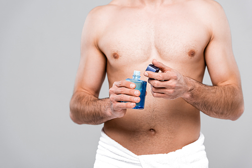 cropped view of muscular man holding bottle with after shave lotion isolated on grey