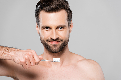 happy and muscular man holding toothbrush isolated on grey
