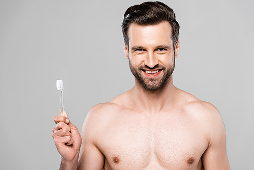 cheerful and muscular man holding toothbrush isolated on grey