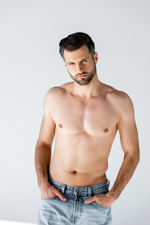 handsome and shirtless man standing with hands in pockets on grey