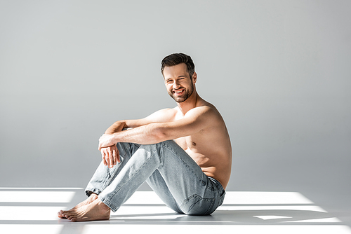 sunshine on happy and shirtless man in blue jeans sitting on grey