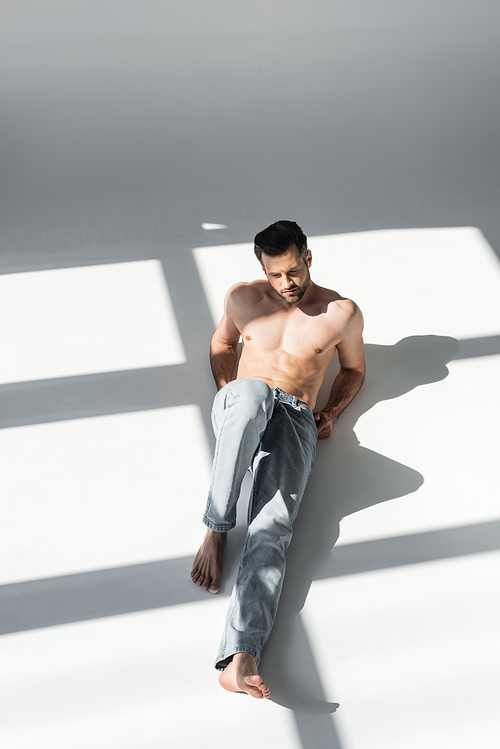 sunshine on muscular man in blue jeans sitting on grey