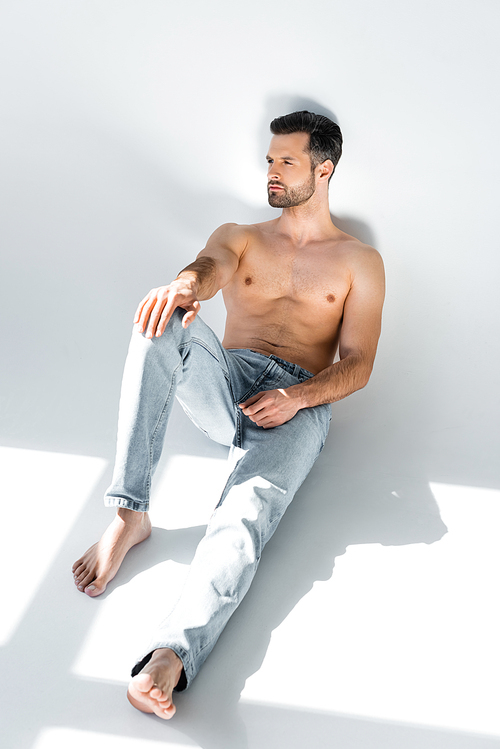 sunshine on muscular man in blue denim jeans sitting on grey