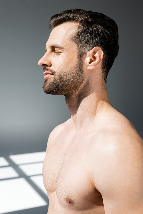 side view of handsome and shirtless man with closed eyes on grey