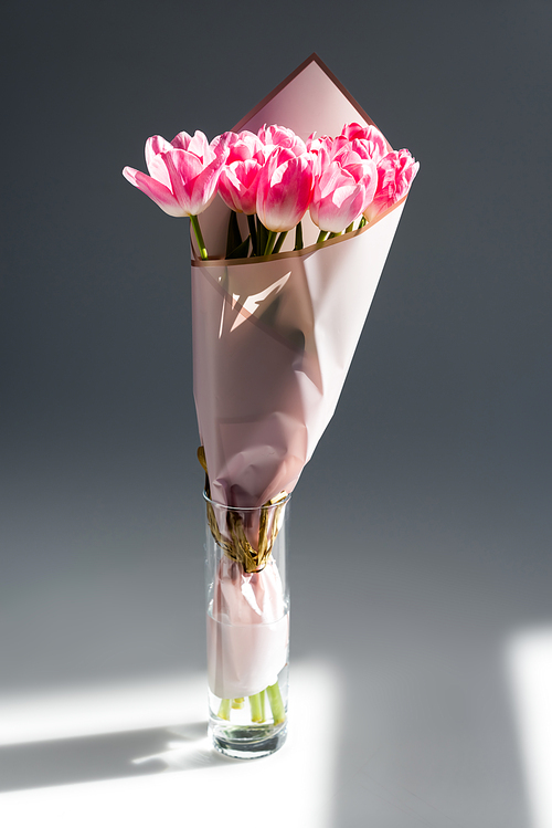 sunlight on pink and blooming tulips in vase with water on grey, mothers day concept
