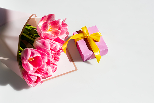 sunlight on pink tulips near gift box on white, mothers day concept