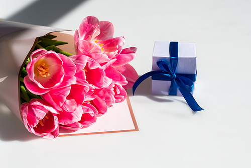 bouquet of pink tulips near small gift box on white, mothers day concept