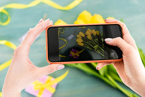 selective focus of woman taking photo of yellow tulips, present and mom tag lettering  on textured surface, mothers day concept