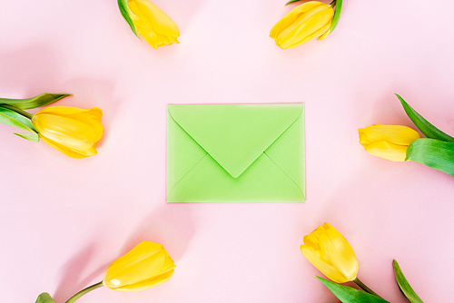 top view of green envelope near yellow tulips on pink, mothers day concept