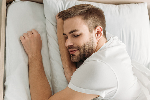 top view of young man smiling while sleeping on white bedding