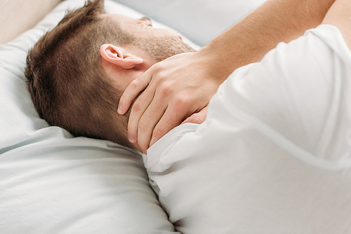 young man lying in bed and suffering from neck pain