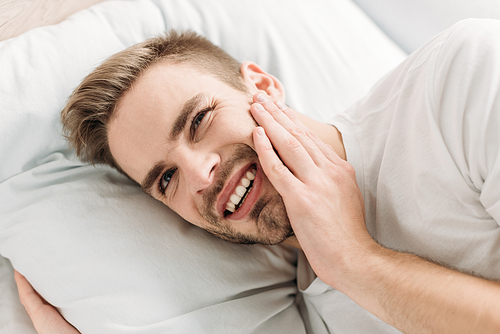 young man lying in bed and suffering from toothache