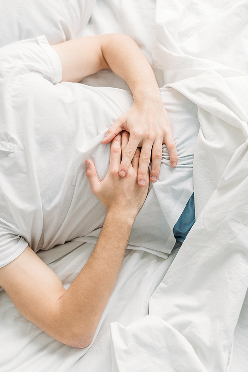 cropped view of man lying on white bedding and suffering from abdominal pain