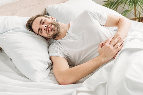 young man lying in bed and suffering from stomach pain with closed eyes