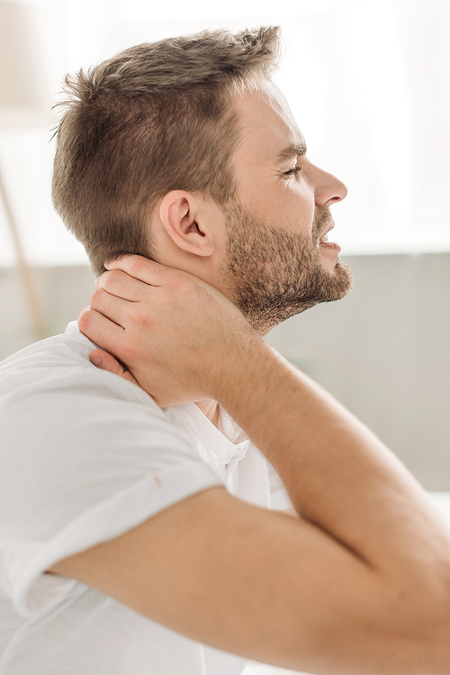 side view of young man touching neck while suffering from pain with closed eyes