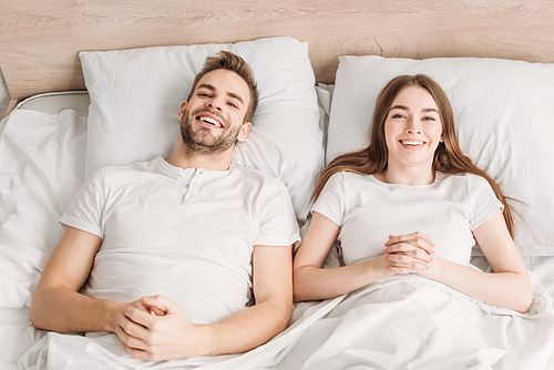 top view of cheerful husband and wife lying in bed and smiling at camera