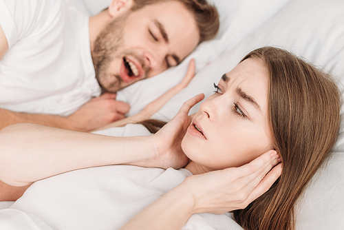 selective focus of woman  ears with hands while lying in bed near snoring husband