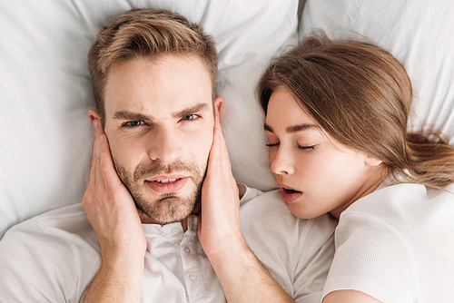 displeased man  ears with hands and  while lying in bed near snoring wife