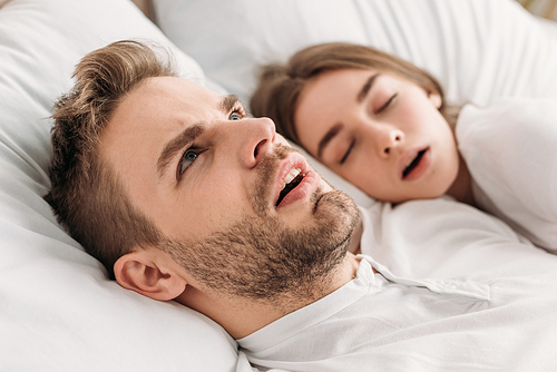 awakened man looking up while lying in bed near snoring wife