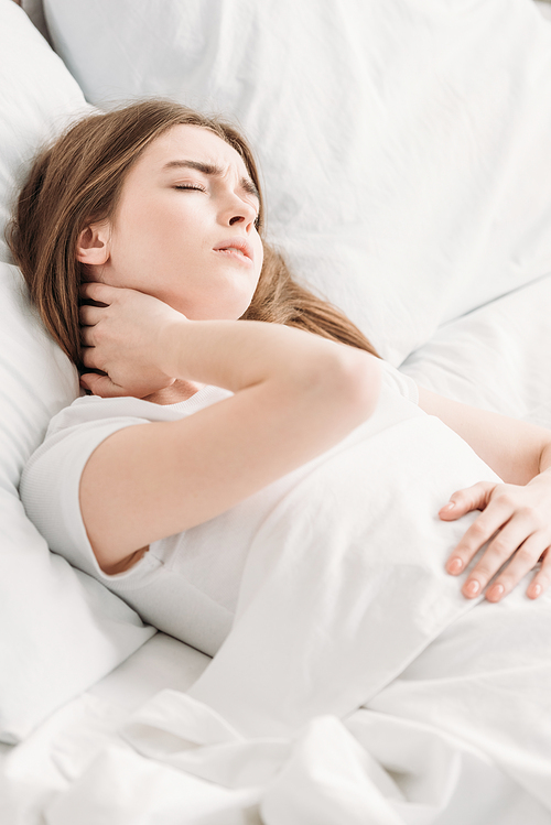 young woman lying in bed with closed eyes while suffering from neck pain