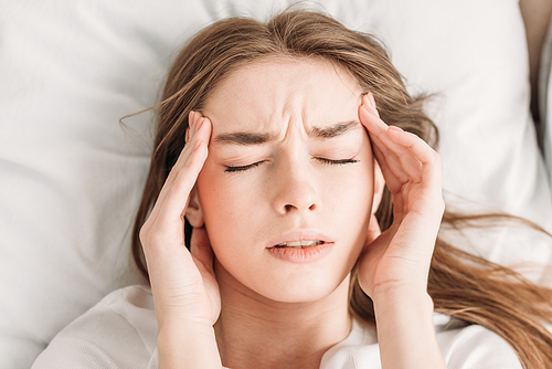 top view of young woman with closed eyes touching head while suffering from migraine