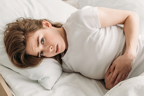 frowned girl  while lying in bed and suffering from abdominal pain